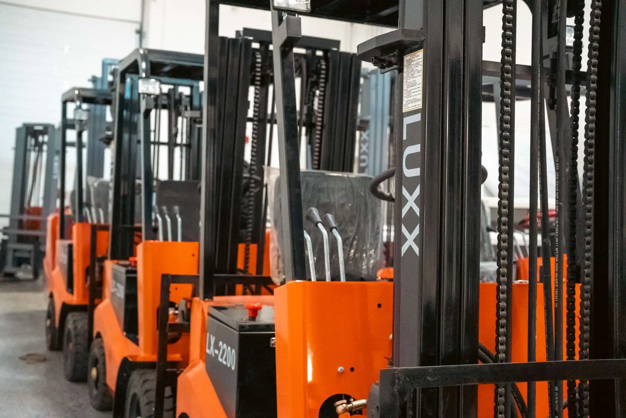 Row of LUXX LX-2200 electric forklifts lined up in a warehouse facility, highlighting the dual-mast chain systems and operator cabins central to routine electric forklift maintenance.