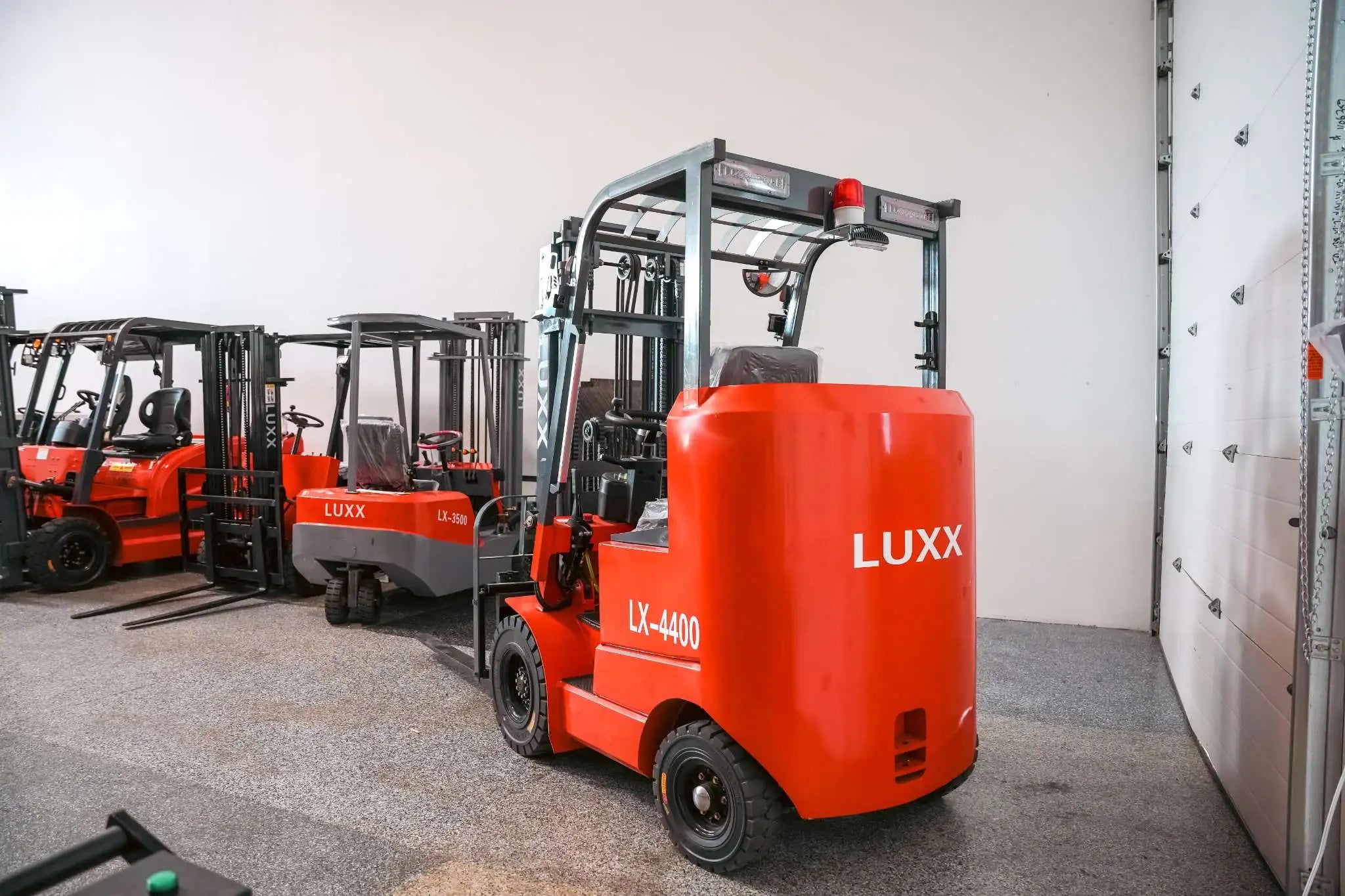 Rear view of the LUXX LX-4400 Compact red forklift showing the branded counterweight, red beacon light, and overhead guard, with LX-3500 and other LUXX models lined up behind.