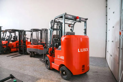 Rear view of the LUXX LX-4400 Compact red forklift showing the branded counterweight, red beacon light, and overhead guard, with LX-3500 and other LUXX models lined up behind.