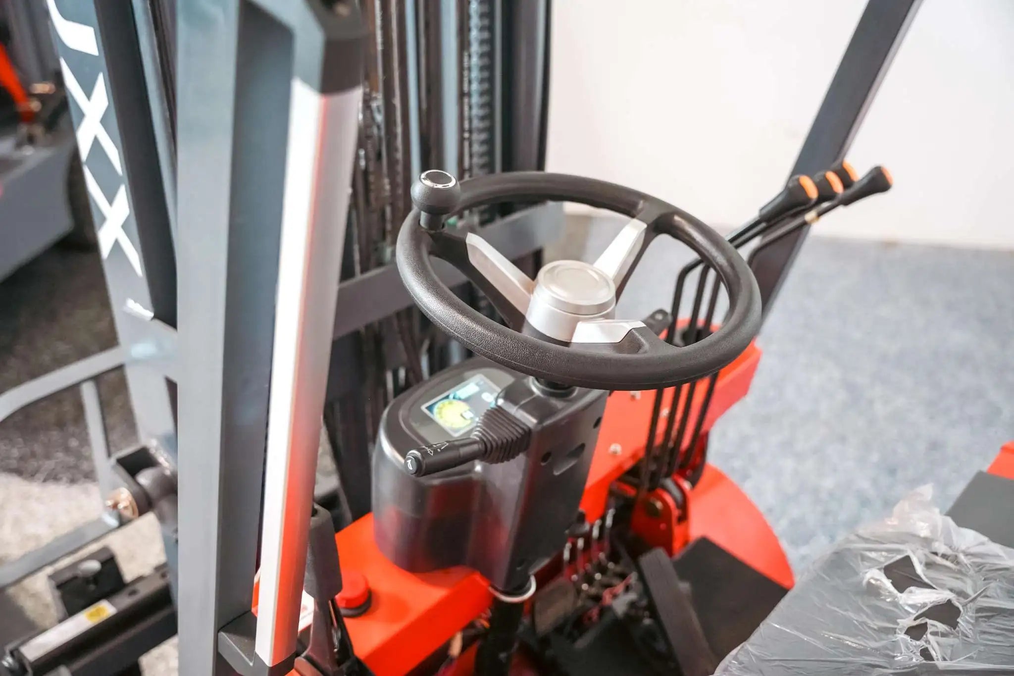 Close-up of the LUXX LX-4400 Compact forklift operator controls showing the three-spoke steering wheel, digital display, joystick, and orange-tipped hydraulic levers.