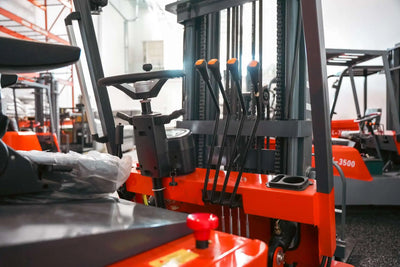 LUXX LX-4400 Compact forklift cabin detail showing orange-tipped hydraulic levers, red emergency stop button, steering column, and mast chains in a large warehouse facility.