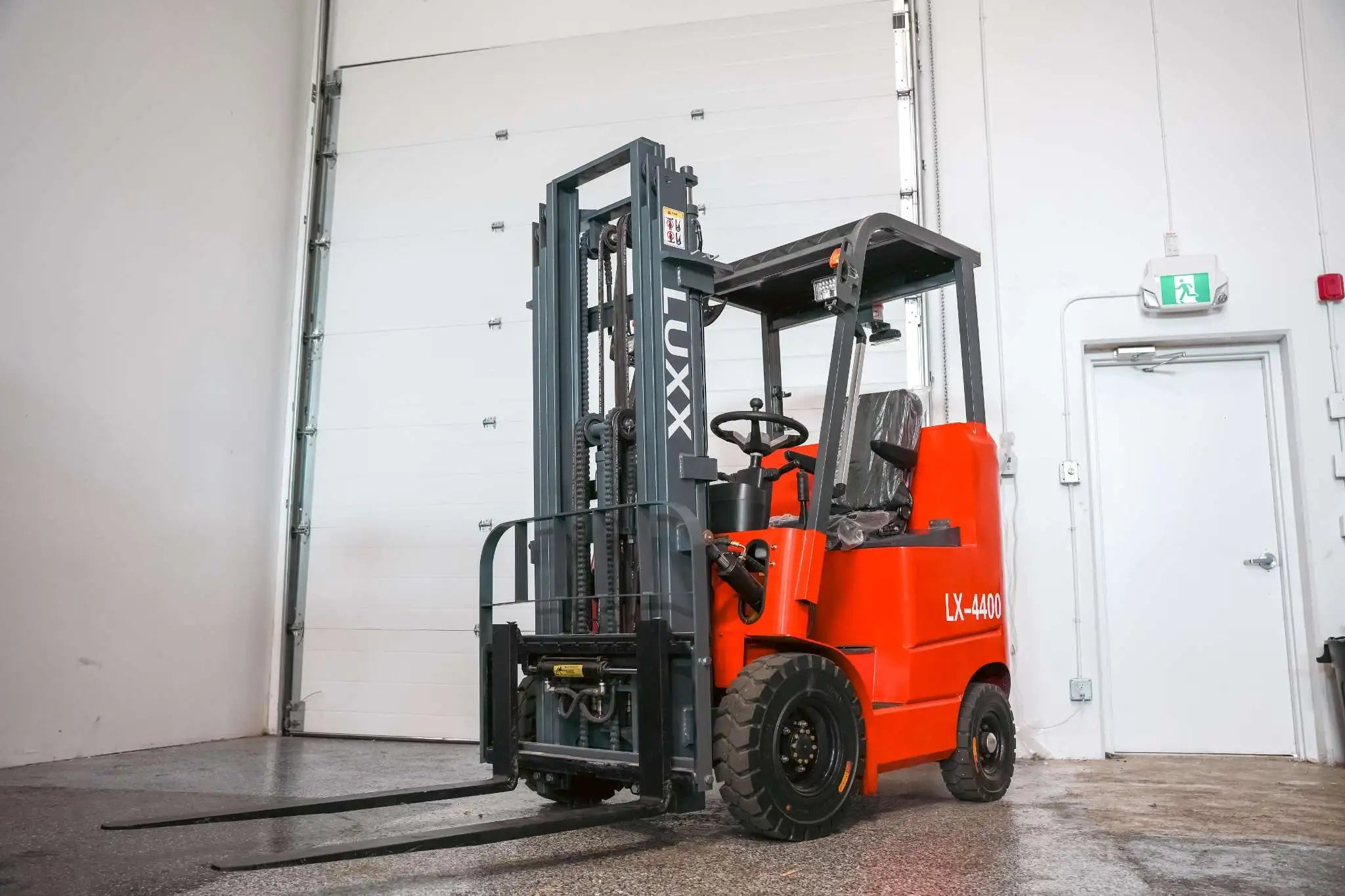 LX-4400 Compact Alt Text: Full front three-quarter view of the LUXX LX-4400 Compact red forklift with extended forks, tall grey dual-mast, and enclosed overhead guard positioned in a clean warehouse bay.