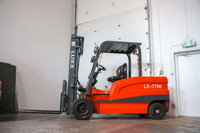 LUXX LX-7700 red forklift with grey mast, overhead guard, and solid tyres, photographed from the side inside an industrial warehouse facility.
