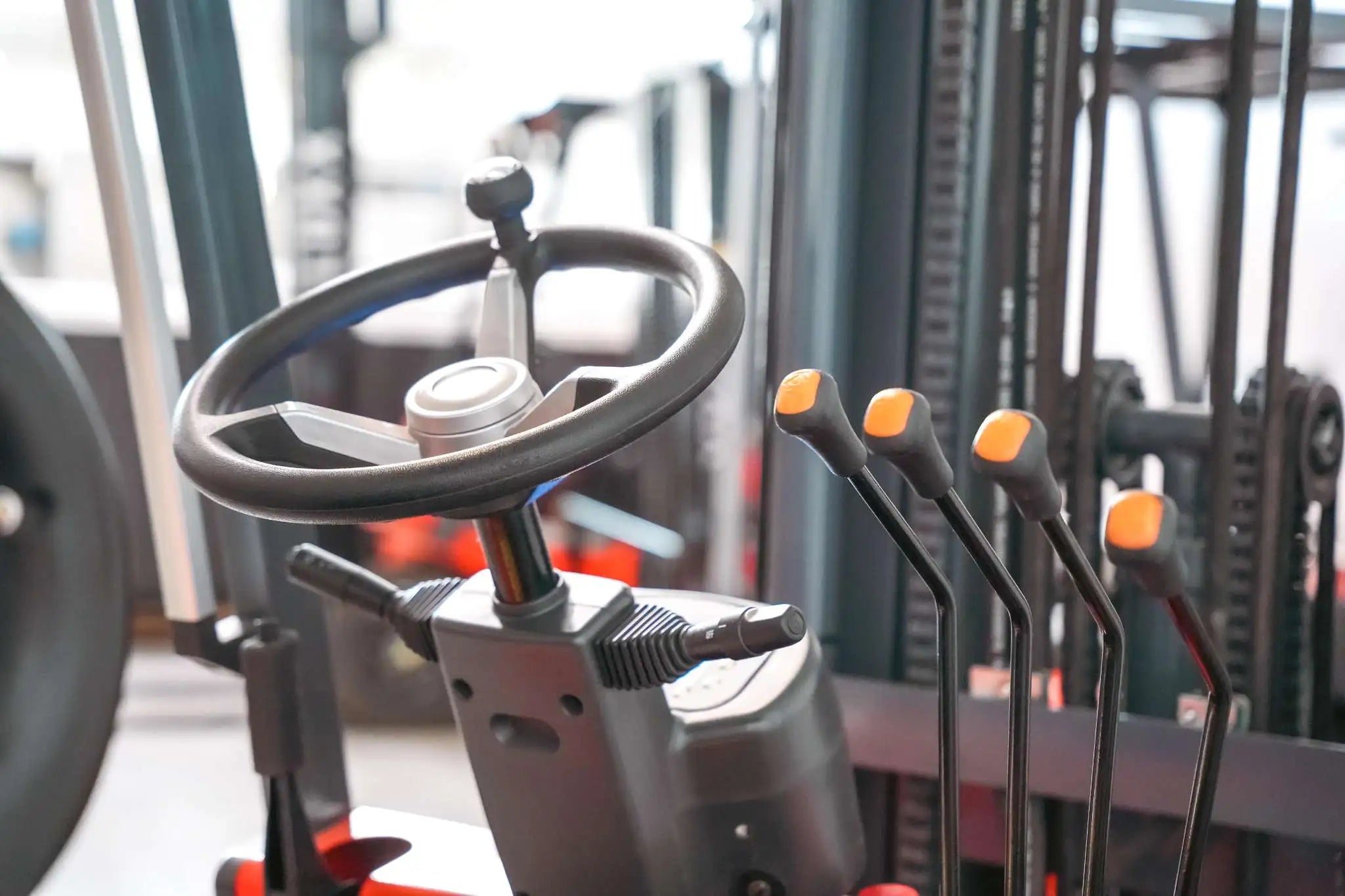 LUXX LX-7700 forklift steering wheel and orange-tipped hydraulic control levers close-up, showcasing the ergonomic operator controls and mast chain system in background.