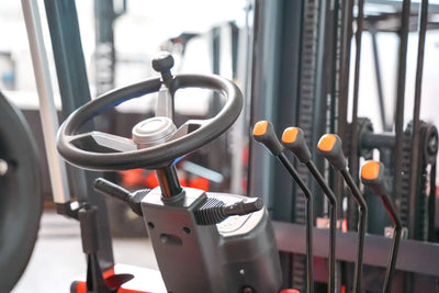 LUXX LX-7700 forklift steering wheel and orange-tipped hydraulic control levers close-up, showcasing the ergonomic operator controls and mast chain system in background.
