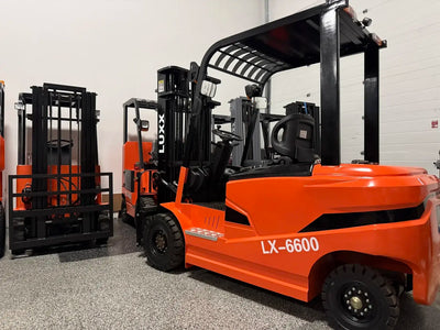 LUXX LX-6600 large orange forklift with wide overhead guard and solid tyres, photographed from a front angle in a showroom with additional LUXX units in the background.
